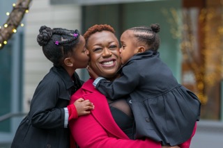 Mom embracing 4 year old daughter while 6 years old daughter is hugging her from behind.