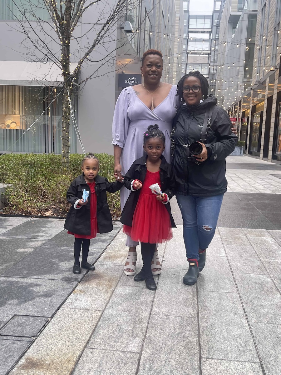 Mom standing next to photographer while 4 and 6 years old daughters are standing in front looking at camera after photo session.