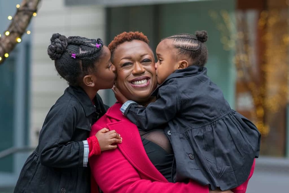 Mother smiling embracing 4 year old daughter while 6 year old daughter is hugging her from behind.